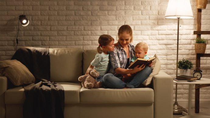 Family before going to bed mother reads children a book about a lamp in the evening
