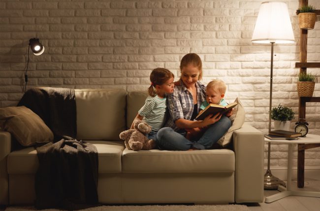 Family before going to bed mother reads children a book about a lamp in the evening
